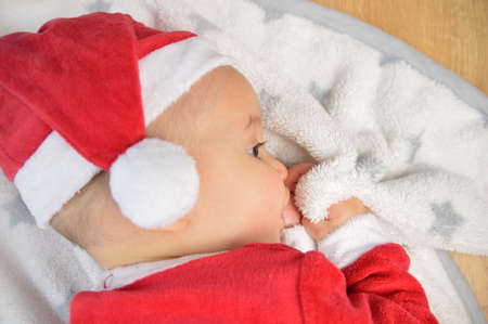 A cute newborn baby in white clothes sleeping in a basket on the floor against a twinkling Christmas Tree with decoration. New Year's Eve.の写真素材