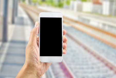 man hand holding a smart phone in a train stationの写真素材