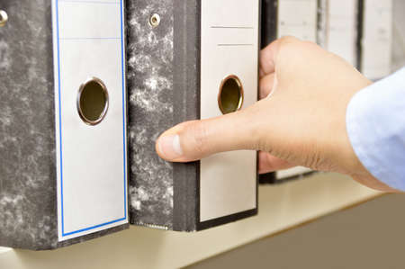 Hand of a businessman going through files on shelves in an officeの写真素材