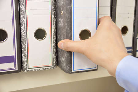 Hand of a businessman going through files on shelves in an officeの写真素材