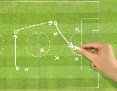 hand of a football coach drawing a tactics of soccer game with white chalk on field backgroundの写真素材