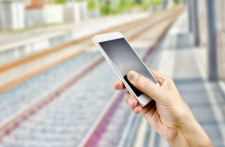man hand holding a smart phone in a train stationの写真素材