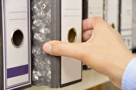 Hand of a businessman going through files on shelves in an officeの写真素材