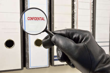 Thief with magnifying glass looking for confidential files at officeの写真素材