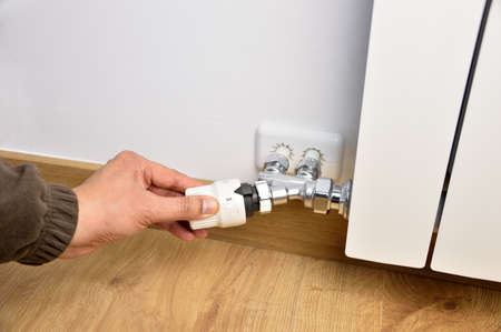 Man's hand adjust thermostat valve close up at homeの写真素材