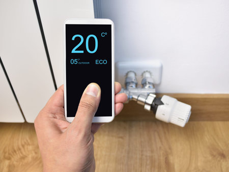 Close up of a person hand adjusting temperature on thermostat through smart phone at home