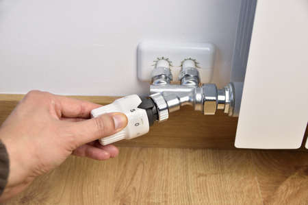 Man's hand adjust thermostat valve close up at homeの写真素材
