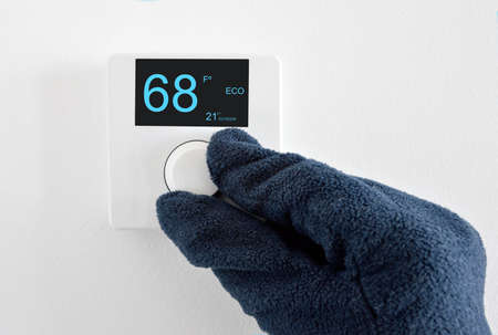Man's hand with glove adjust thermostat digital in fahrenheit at homeの写真素材