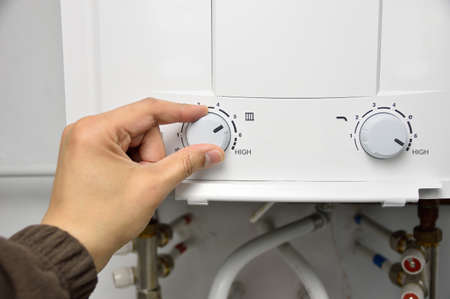 Man's hand rotate temperature adjuster of water heater. High tempの写真素材