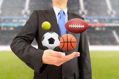 Business man with group of balls of different sports in hand at stadiumの写真素材