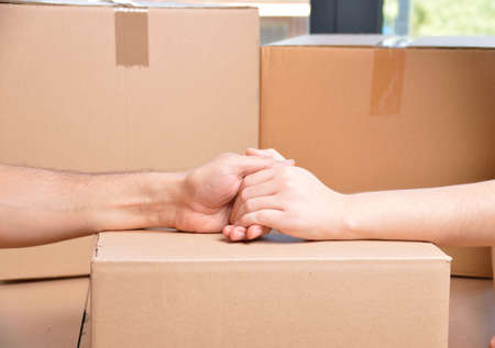 Close up of a couple holding hands over a carton box and moving homeの写真素材