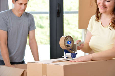 Close up of a happy couple moving home packing boxes and sealing with tape sitting on the floorの写真素材
