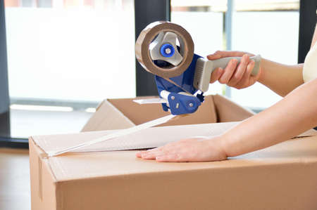 Shot of an unidentifiable young woman closing a cardboard box with tape at homeの写真素材