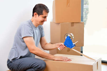 Shot of an man closing a cardboard box with tape at homeの写真素材
