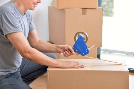 Shot of an man closing a cardboard box with tape at homeの写真素材