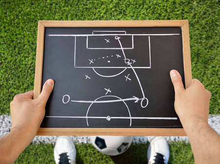 hand of a football coach drawing a tactics of soccer game with white chalk on blackboard at stadium backgroundの写真素材