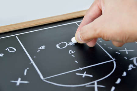 hand of a basketball coach drawing a game tactics with white chalk on blackboardの写真素材