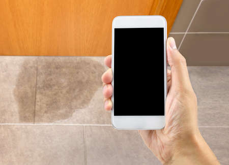 A hand holding a smartphone to call the professional to repair a water leak in the roomの写真素材