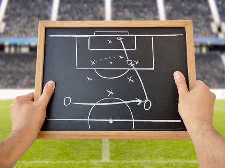 hand of a football coach drawing a tactics of soccer game with white chalk on blackboard at stadium backgroundの写真素材