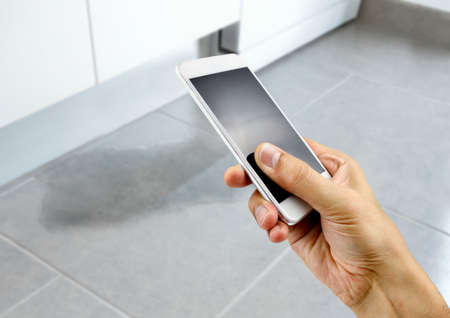 A hand holding a smartphone to call the professional to repair a water leak in the kitchen roomの写真素材
