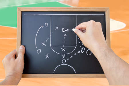 hand of a basketball coach drawing a game tactics with white chalk on blackboard at stadiumの写真素材