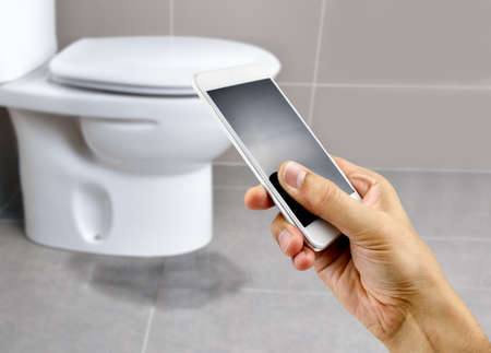 A hand holding a smartphone to call the professional to repair a water leak in the toiletの写真素材