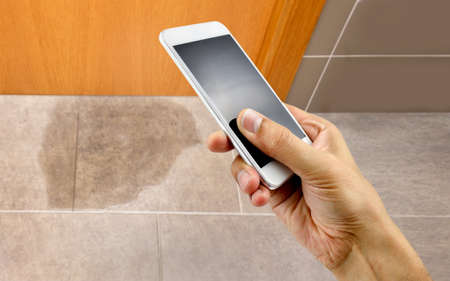 A hand holding a smartphone to call the professional to repair a water leak in the roomの写真素材