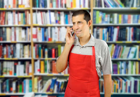 shop man with apron uses a smartphone at bookshopの写真素材