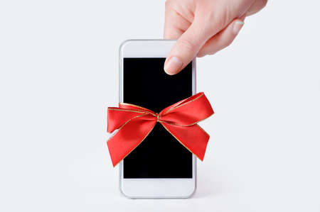 hand holding a phone gift with a red ribbon and white backgroundの写真素材