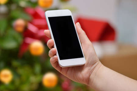 Hand showing a smart phone with a Christmas tree background at homeの写真素材