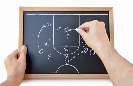 hand of a basketball coach drawing a game tactics with white chalk on blackboard over white backgroundの写真素材