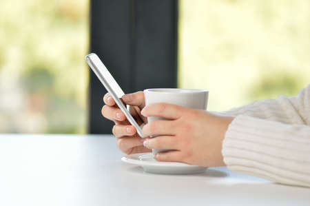 Closeup shot of an unrecognizable woman having a cup of coffee at a cafe and using a phoneの写真素材