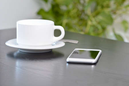 Closeup shot of a cellphone and drinking a coffee at homeの写真素材