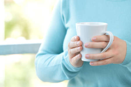 Woman hands holding a coffee mug at homeの写真素材