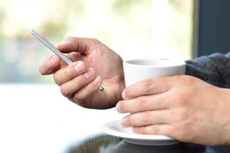 Hands holding coffee and using smart phone at homeの写真素材