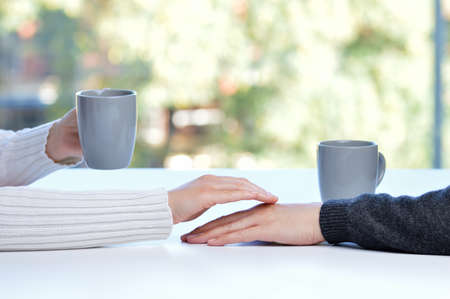 Close up of a woman touching the hand of her partner during a date in a table of a coffee shop or homeの写真素材