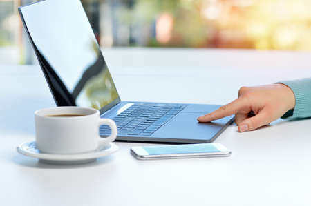 Back light close up of a lady hand browsing websites in a laptop sitting in a desktop in a house の写真素材