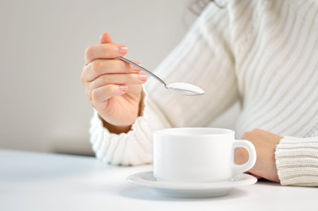 Hand of woman throwing sugar into coffee with a spoon