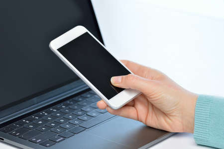 Girl hands using a smart phone and a laptop on a desk at officeの写真素材