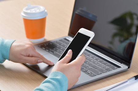 Girl hands using a smart phone and a laptop on a desk with a coffee drink