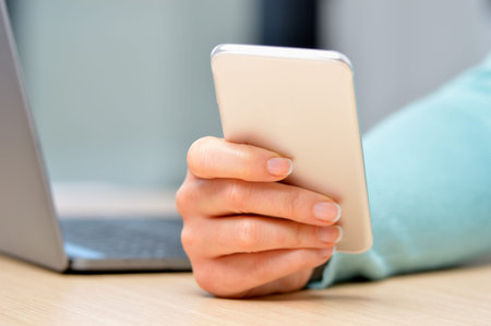 Close up of a woman hand using a silver smart phone on a desk at home