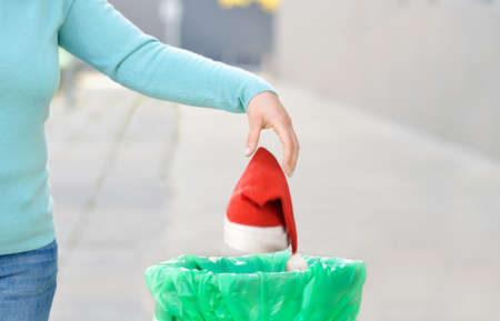 Woman throwing a santa hat to the trash in a trash bin a city after Christmasの写真素材