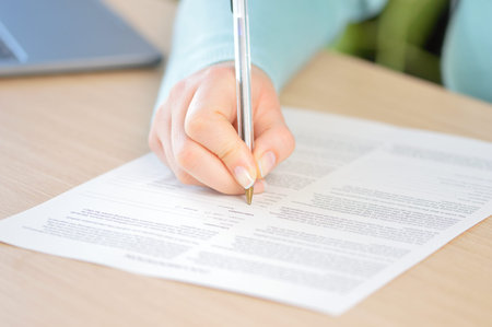 Close up of a woman hand writing or signing in a document on a desk at home or office