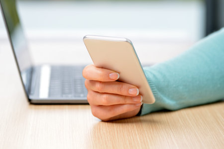 Close up of a woman hand using a silver smart phone on a desk at homeの写真素材