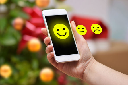 Woman pressing happy icon a smart phone with a Christmas tree background at home