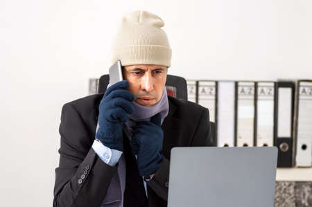 Worried executive who is cold and calls technical service for repair of the heating at officeの写真素材