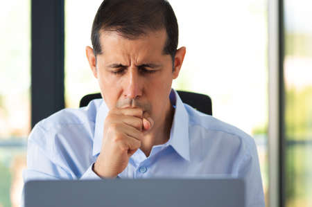 Cropped shot of a handsome young businessman sitting alone in his office and coughing as he suffers from a coldの写真素材