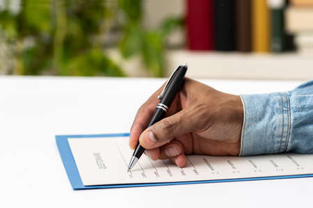 Close up of man hand filling form on a table at home or officeの写真素材