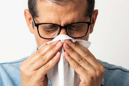 Portrait of a man blowing his nose with a tissue against a white backgroundの写真素材