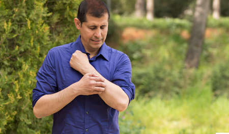 Man scratching arm because it stings in a park with copy spaceの写真素材